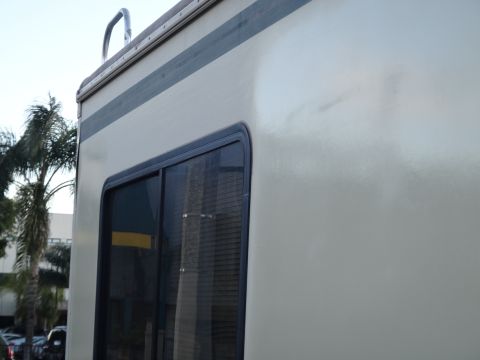 1995 Chevrolet P30 1 Ton - Step Van - The side of a beige step van is shown, featuring a dark-framed window with blinds and a dark stripe near the top. A chrome ladder is visibl…