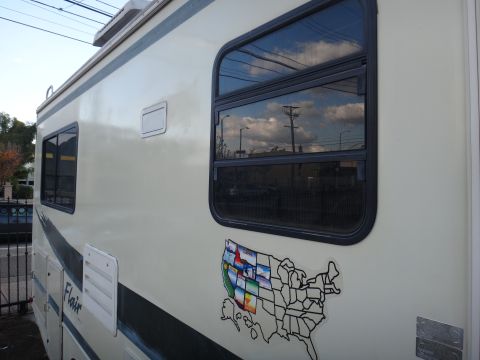 1995 Chevrolet P30 1 Ton - Step Van - The side view of a cream-colored RV shows a large tinted window reflecting the sky and power lines. A sticker of the United States with sta…