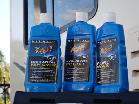 1995 Chevrolet P30 1 Ton - Step Van - Three blue bottles of Meguiar's Marine RV cleaning products are displayed on a dark shelf against a blurred background of a vehicle.