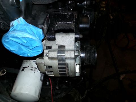1994 Ford Bronco - A close-up view of an alternator and oil filter on a vehicle's engine. Blue painter's tape is covering a component above the alternator.