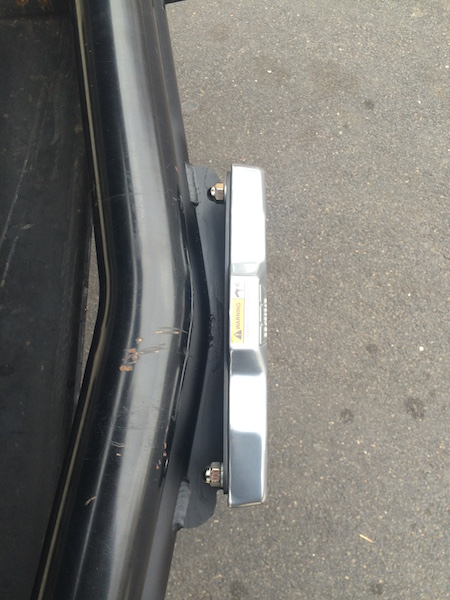 1981 Ford Bronco - A close-up, side view of a chrome-plated rectangular object with a yellow warning sticker, mounted to a black metal frame with bolts. The o…