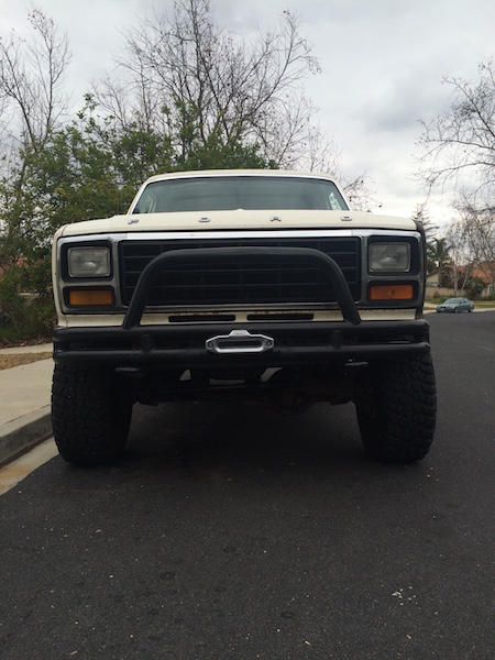 1981 Ford Bronco - Front view of a white Ford truck with a black bull bar and winch mounted on the front bumper. The vehicle is parked on an asphalt road with…