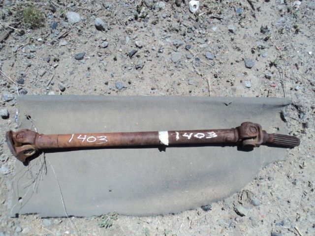 Rusty driveshaft with white markings "1403" on a grey tarp.