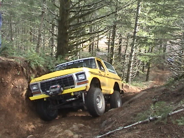 Yellow lifted Ford Bronco with winch bumper crawling a dirt bank in pine woods