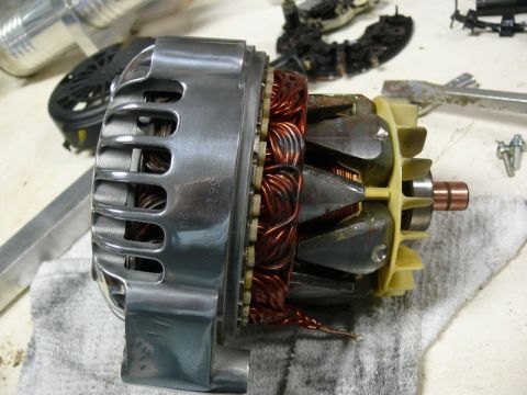 Disassembled automotive alternator with copper windings and fan visible.