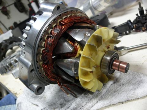 Disassembled automotive alternator with copper windings and yellow fan.