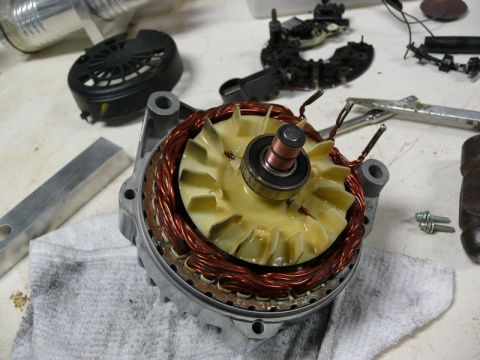 Alternator internal components with copper windings, fan, and bearing. Tools and parts in background.