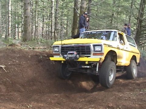 1994 Ford Explorer - Yellow Ford Bronco with winch navigates a dirt incline in a wooded area.