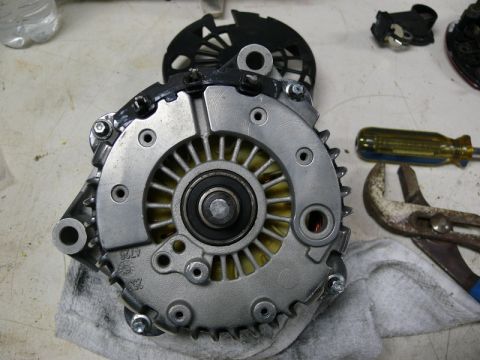 Disassembled automotive alternator with tools on a workbench.