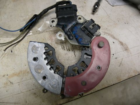 Disassembled car alternator voltage regulator and rectifier assembly on a workbench.