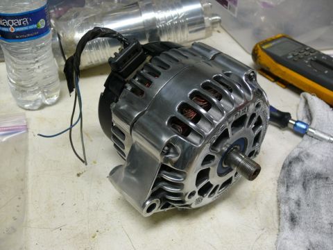 Chrome alternator with exposed copper windings and wires on a workbench.