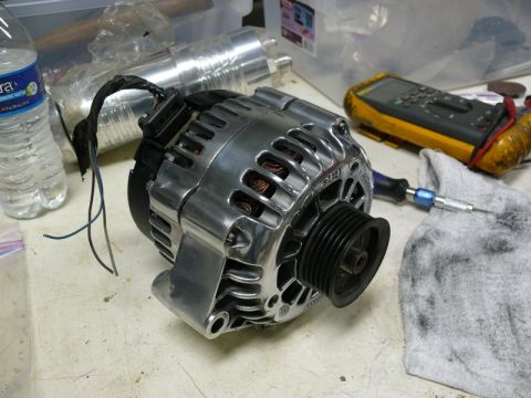 Polished aluminum automotive alternator with black pulley on a workbench.