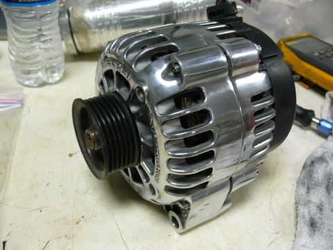 Polished chrome alternator with black pulley on a workbench.
