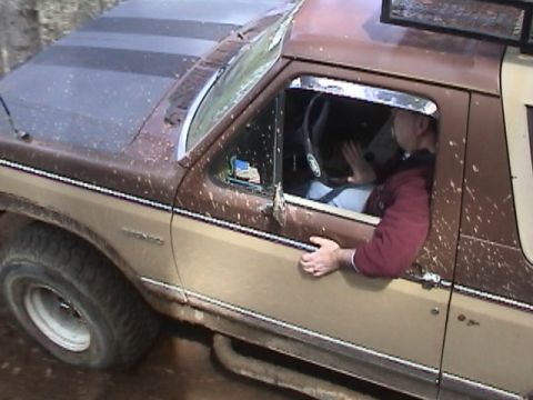 1994 Ford Explorer - A driver is visible inside a mud-covered Ford Bronco as it navigates an off-road trail.