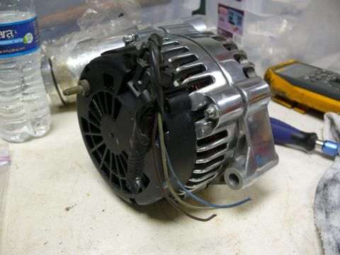 Car alternator with wires and a tool on a workbench.
