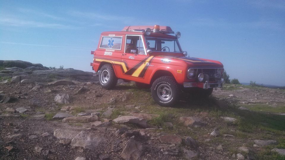 Red 1979 Ford Bronco with racing stripes on a rocky hill.