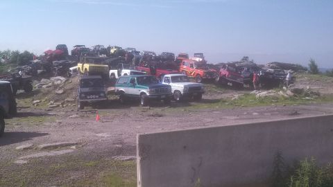 1979 Ford Bronco - A collection of off-road vehicles, including several Ford Broncos and trucks, are parked on a rocky hillside under a clear sky.