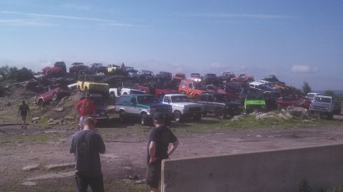 1979 Ford Bronco - A large collection of off-road vehicles, primarily Ford Broncos and similar trucks, are parked on a rocky hillside under a clear blue sky.…