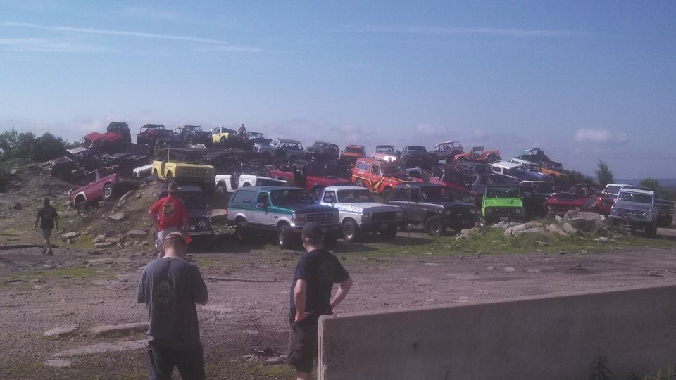 A large group of off-road vehicles, mostly Ford Broncos, parked on a rocky hill.