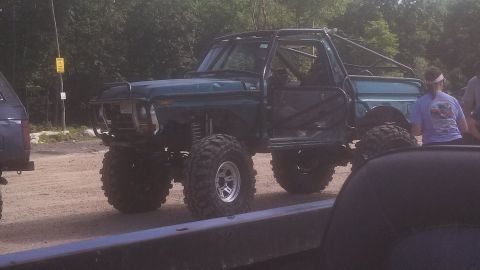 1979 Ford Bronco - A heavily modified, lifted dark green Ford Bronco with a roll cage and large off-road tires sits on a dirt lot. The driver's door is open,…