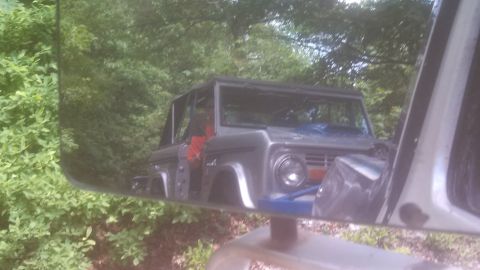 1979 Ford Bronco - A reflection in a side mirror shows the front 3/4 view of a vintage Ford Bronco. The vehicle appears to be silver and is parked outdoors wi…