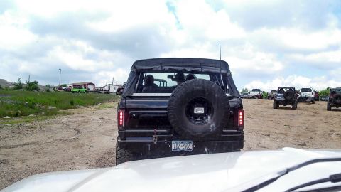 1979 Ford Bronco - The rear view of a black Ford Bronco with a soft top is parked on a dirt lot. A spare tire is mounted on the back, and a New York license p…