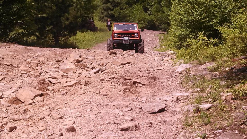 Orange Ford Bronco driving up a rocky off-road trail.