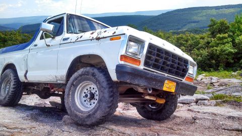 1979 Ford Bronco - A white 1979 Ford Bronco with off-road tires is parked on a rocky terrain with a scenic mountain landscape in the background. The truck sho…