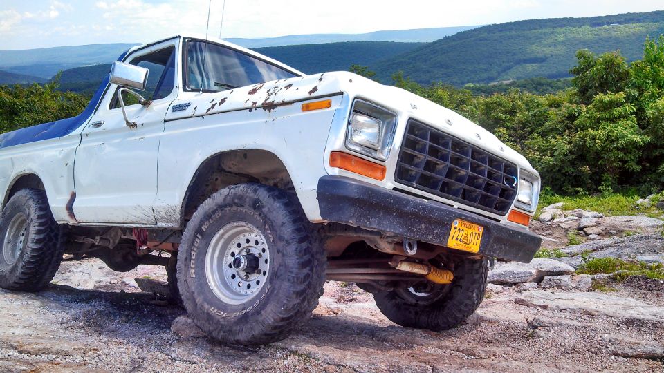 White 1979 Ford Bronco with off-road tires on a rocky mountain overlook.