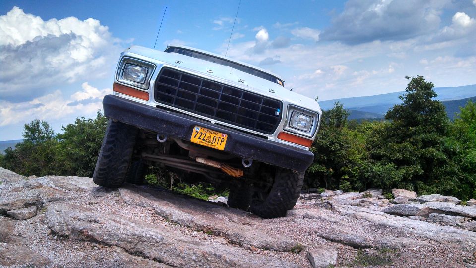 White 1979 Ford Bronco climbing a rocky hill, front view.