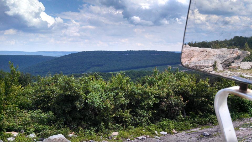 View from a vehicle over mountains, with a side mirror reflecting a rock.