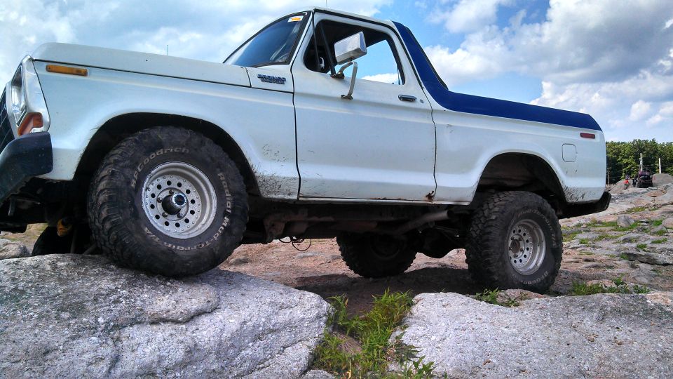 White 1979 Ford Bronco with blue top on rocky terrain, front tire on rock.