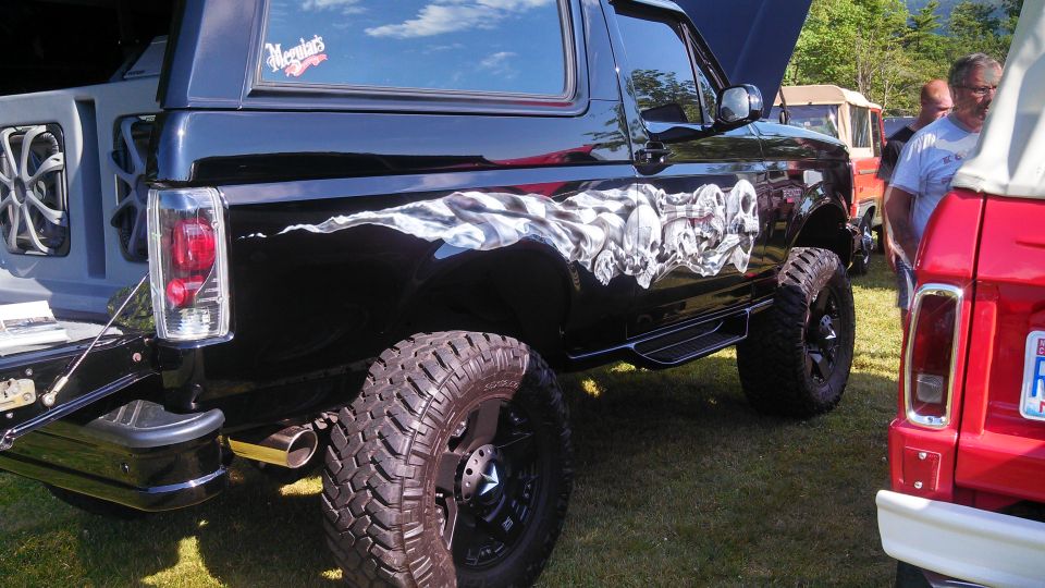 Black lifted Ford Bronco with skull graphic, large off-road tire, chrome exhaust tip.