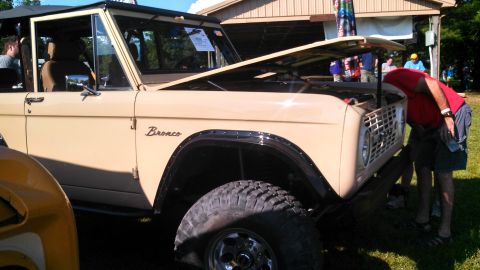 1979 Ford Bronco - A tan 1979 Ford Bronco is parked on a grassy area with its hood open. A person in a red shirt is leaning over the engine bay.