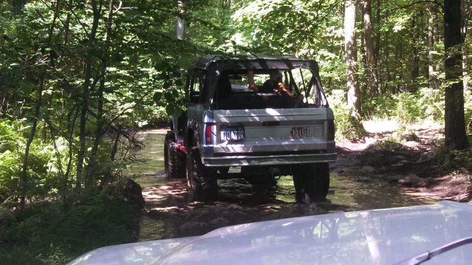 Silver 1979 Ford Bronco driving through a stream in a forest.