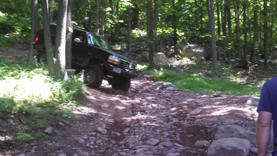 Black Ford Bronco off-roading on a rocky trail in a forest.