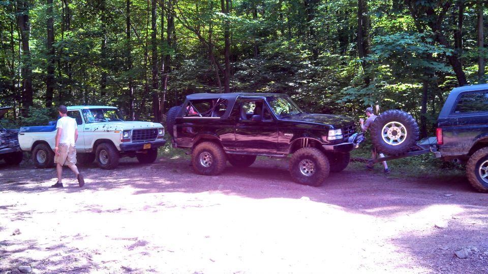 White Ford pickup and black Ford Bronco in woods; Bronco is being towed.