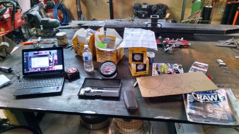 1985 Jeep CJ7 - A workbench is cluttered with tools, gauges, a laptop, and magazines. A chainsaw and a vise are visible in the background.
