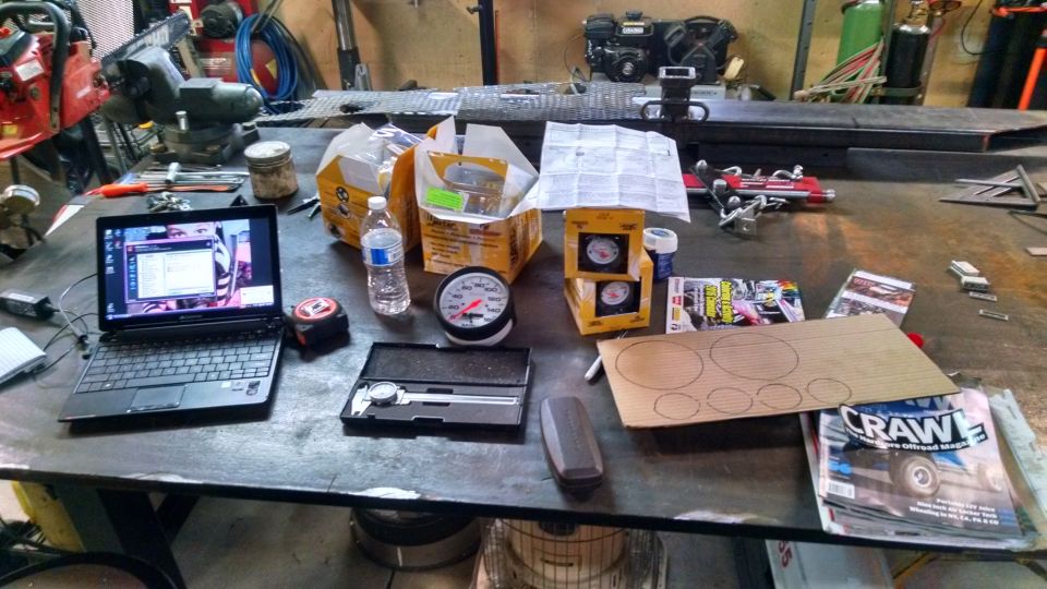 Workbench with tools, gauges, laptop, and magazines.