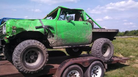 1979 Ford Bronco - A heavily modified, bright green off-road truck with large tires is loaded onto a rusty trailer. The truck's body is dented and appears to…
