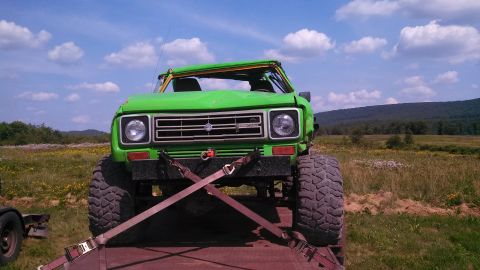 1979 Ford Bronco - A bright green, lifted off-road vehicle is secured with straps to a trailer in a grassy field under a blue sky with scattered clouds. The v…