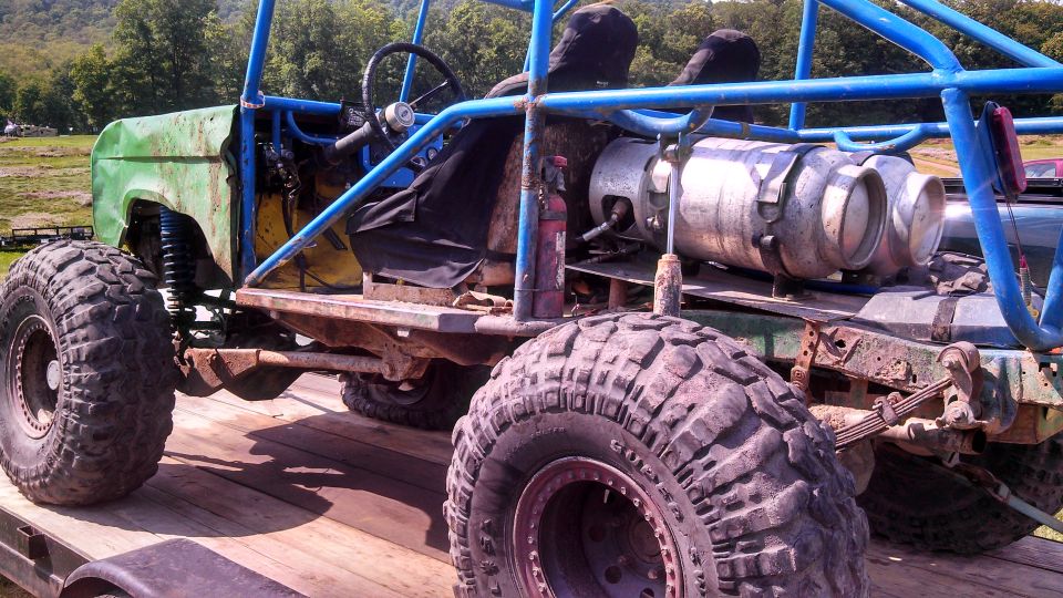Custom off-road vehicle with blue roll cage and large tires on a trailer.