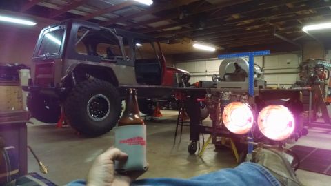 1985 Jeep CJ7 - A person holds a beer in a koozie in front of a modified Jeep CJ7 in a garage. The Jeep is lifted with large tires and appears to be underg…