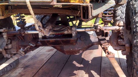 1979 Ford Bronco - The underside of a heavily modified off-road vehicle shows a rusted differential, suspension components including blue-sprung shocks, and a…