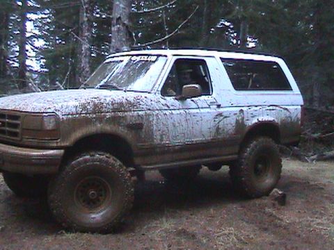 1994 Ford Explorer - This white SUV, likely a 1992 Ford Bronco, is heavily covered in mud after an off-road excursion. A sticker on the windshield indicates mem…