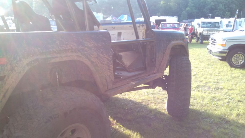 Muddy 1979 Ford Bronco with doors removed, showing interior and roll cage. Other vehicles and tents in background.
