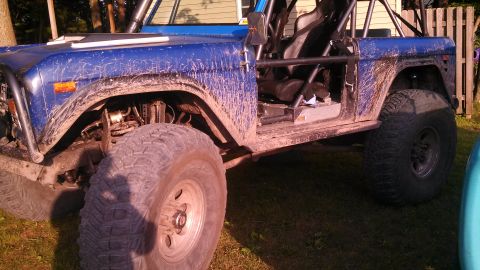 1979 Ford Bronco - The side view of a blue, mud-covered 1979 Ford Bronco is shown with a roll cage, off-road tires, and a removed door. The vehicle is parked…