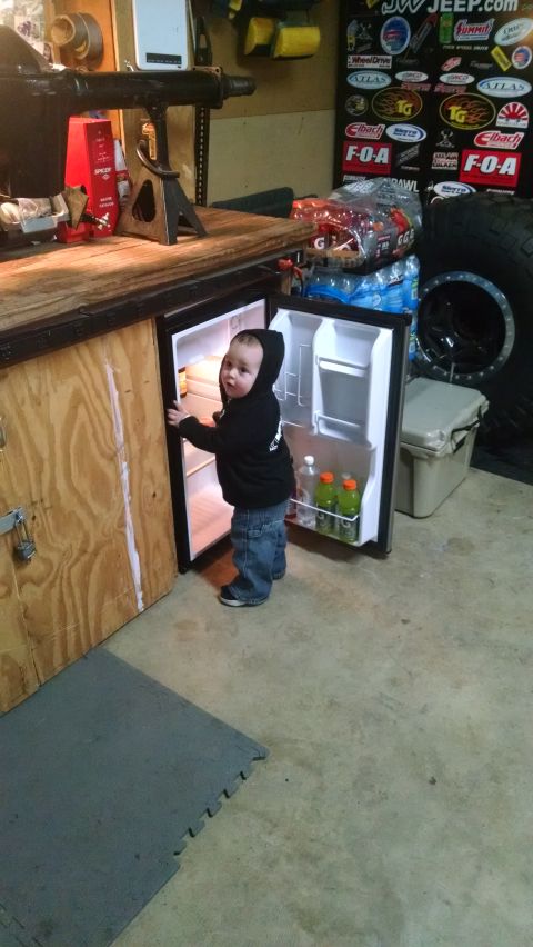 1985 Jeep CJ7 - A toddler in a black hoodie and jeans stands in front of an open mini-fridge, looking at the camera. The fridge is stocked with drinks and…