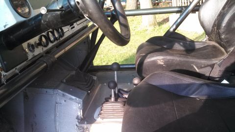 1979 Ford Bronco - The interior of a vehicle shows a steering wheel, dashboard with gauges, and two black bucket seats. Multiple gear shifters are visible in…