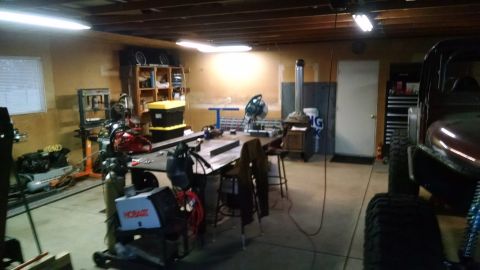 1985 Jeep CJ7 - A dark red Jeep CJ7 is parked in a workshop, partially obscured by a large tire in the foreground. The workshop contains various tools and…